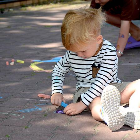 Mały chłopiec maluje kredami po chodniku 