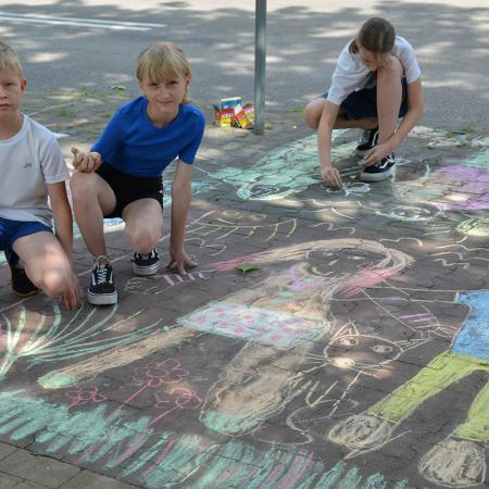 Dzieci pokazują wykonane rysunki na chodniku