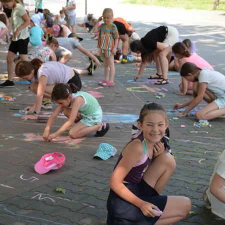 Grupa dzieci maluje kredami po chodniku 