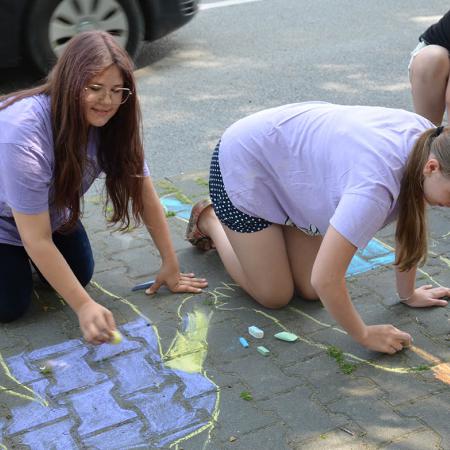 dziewczyny malują kolorowe postaci na chodniku przed RCK 