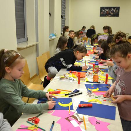 Duża grupa dzieci siedzi przy stołach i robi dekoracje z papieru kolorowego