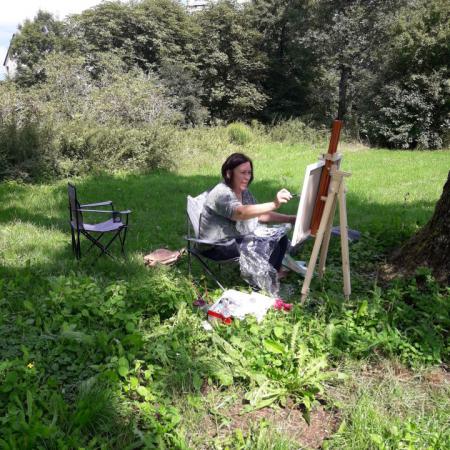 Kobieta siedzi pod drzewem i maluje obraz 
