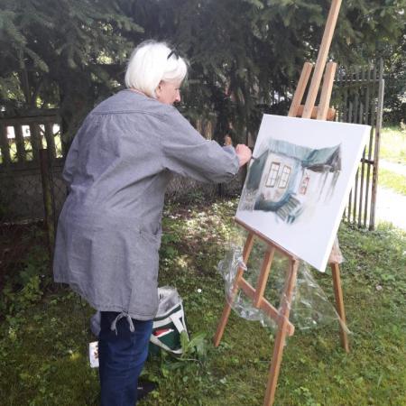 Kobieta maluje obraz przedstawiający Dworek w Drzewicy