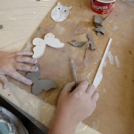 Ręce dziecka na stole modelujące kształt motyla Obok glina szablony i woda w kubku