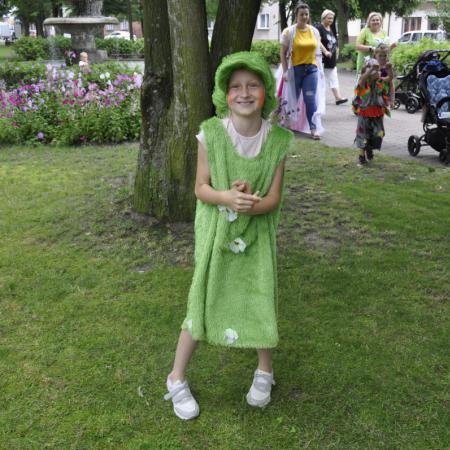 Dziewczynka ubrana cała na zielono stoi w parku w tle ludzie
