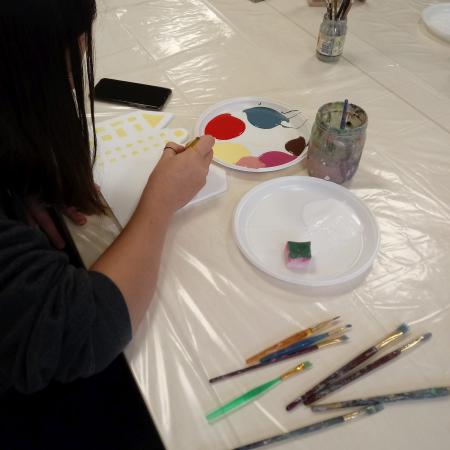 Dziewczyna maluje farbami obok słoik, pędzelki i farby