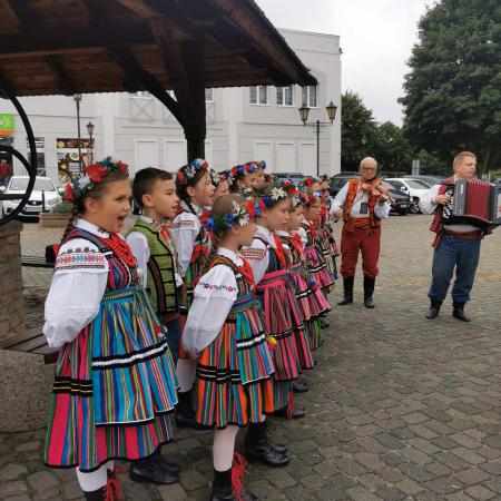 Grupa dzieci w ludowych strojach śpiewa na rynku 
