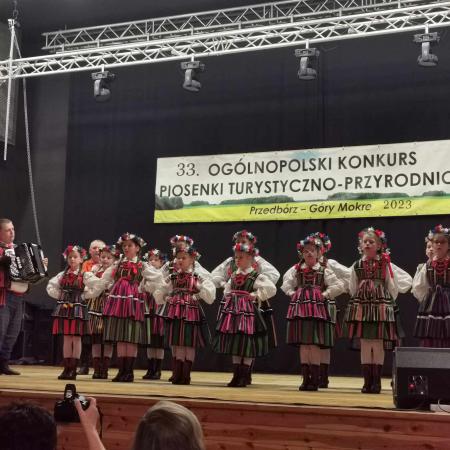Grupa dzieci w ludowych strojach śpiewa na scenie podczas Konkursu Piosenki Turystyczno-Przyrodniczej