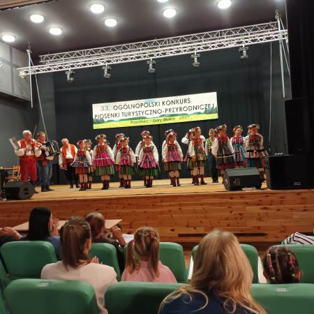 Grupa dzieci w ludowych strojach śpiewa na scenie 