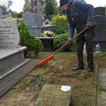 Mężczyzna grabi plac przy zabytkowym grobie na cmentarzu w Drzewicy