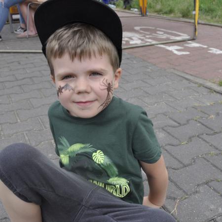 Chłopiec w czapce z pomalowaną twarzą siedzący na chodniku