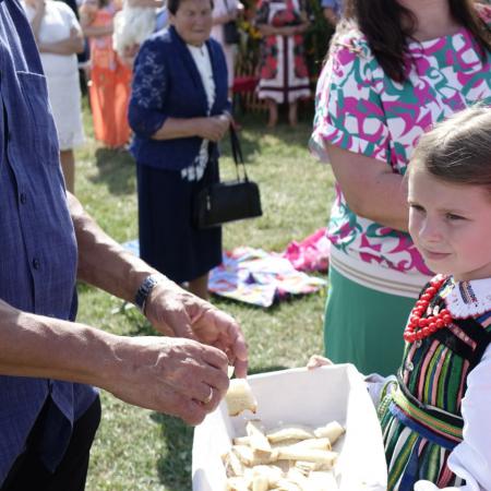 Dziewczynki w ludowych strojach dzielą chlebem zgromadzonych ludzi na Mszy świętej