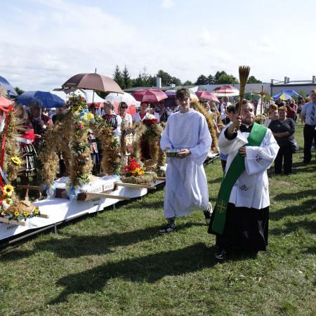 Ksiądz z kropidłem święci plony 