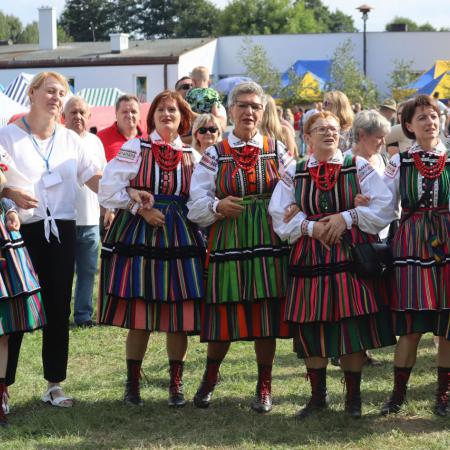 Grupa osób w ludowych strojach stoi w rzędzie przed sceną na dożynkach w Jelni