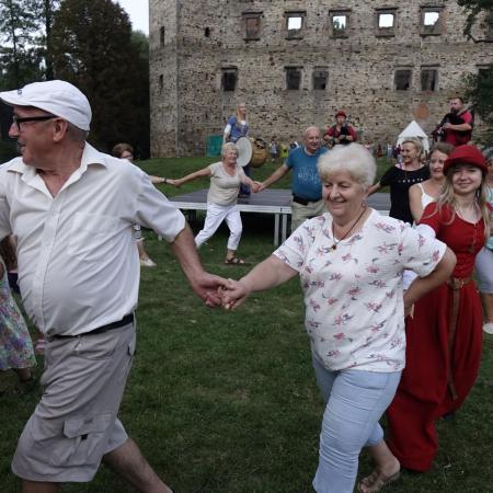 Grupa ludzi tańczy w kółku przy zamku 