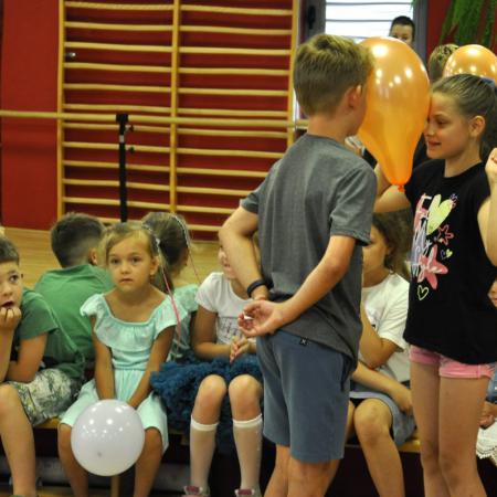 Chłopiec i dziewczynka w tańcu z balonem, za nimi siedzące dzieci