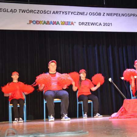 Cztery osoby w czerwonych strojach z pomponami występują na scenie