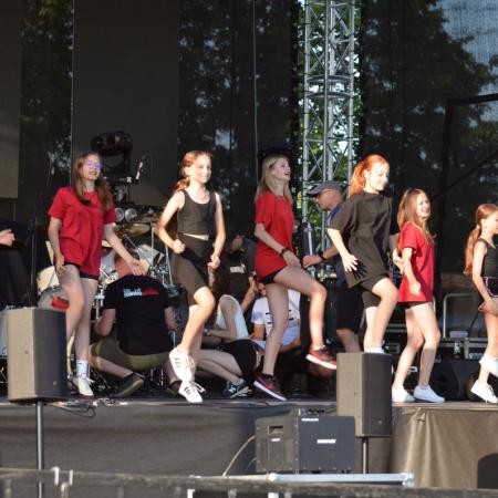 Uczestniczki zajęć tanecznych występują na scenie w czerwonych i czarnych koszulkach