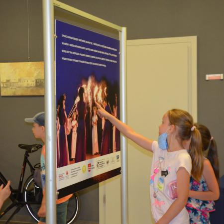 Dziewczynki oglądające wystawe, jedna z nich wskazuje zdjęcie na planszy wystawienniczej.