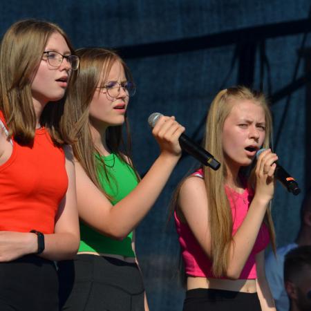 Dziewczyny w kolorowych koszulkach śpiewają na scenie przy mikrofonach