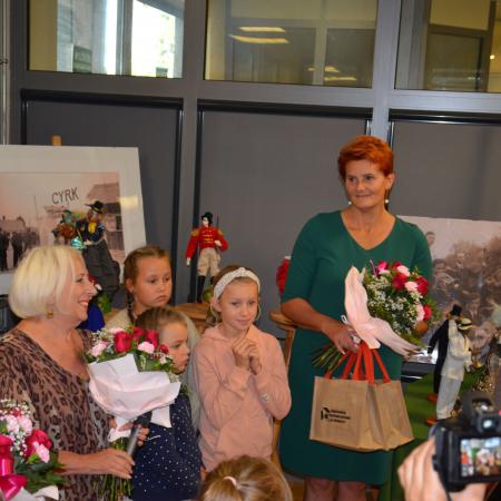 Dwie kobiety trzymają kwiaty , obok ich stoją dzieci zaproszone na wystawę Lalek Artystycznych w RCK