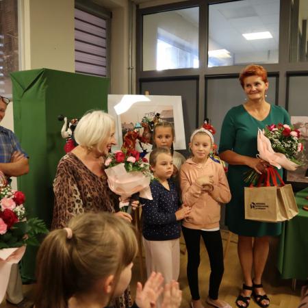 Dyrektor RCK i Autorka wystawy stoją z kwiatami obok nich zaproszone dzieci i dorośli 