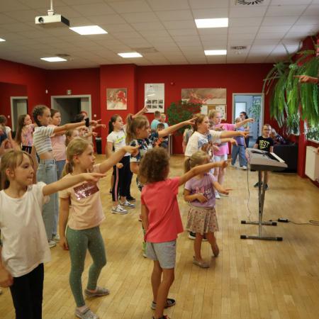 Grupa dzieci tańczy do ruchów pokazywanych przez instruktora zajęć wakacyjnych
