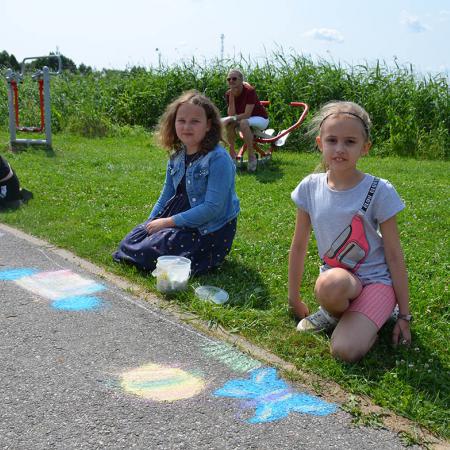 Dwie dziewczynki malują kredami po asfalcie