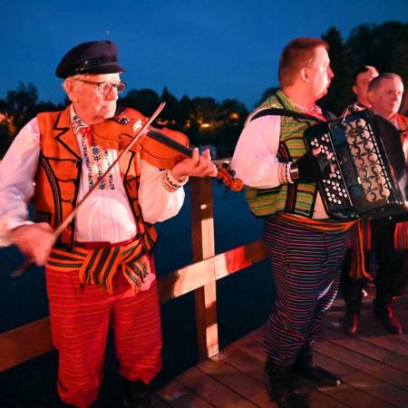 Instrumentaliści z zespołu ludowego wykonują piosenki ludowe.