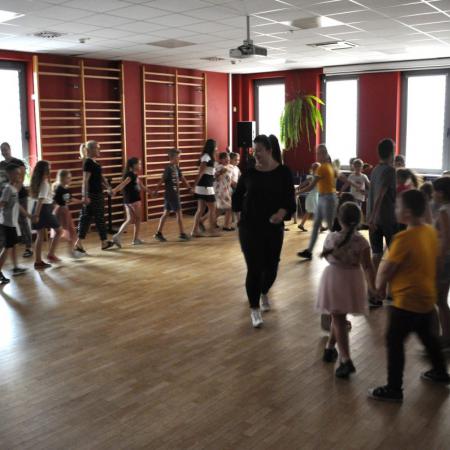 Duża grupa dzieci wraz z instruktorami trzyma się za ręce i tańczy