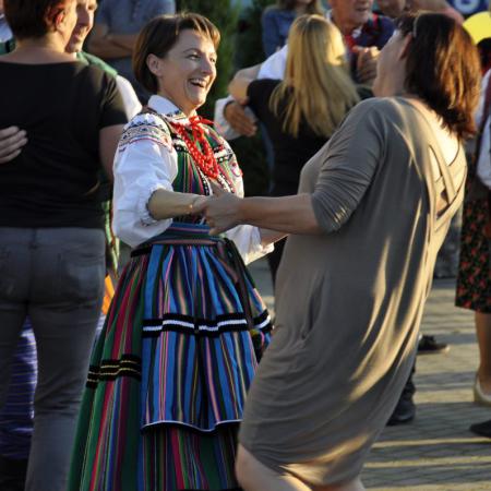 Dwie kobiety śmieją sie i tańczą ,w tle grupa bawiących się ludzi.