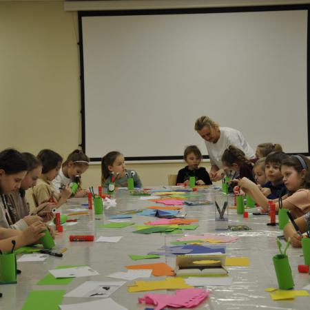 Dzieci siedzą przy stole i robią żaby z papieru kolorowego