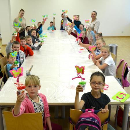Dzieci z klasy drugiej i trzeciej siedzą przy stole w rękach trzymają wykonane prace plastyczne