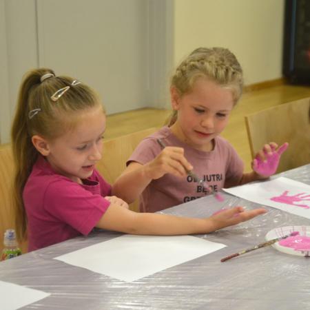 Dziewczyna  maluje koleżance dłonie różową farbą