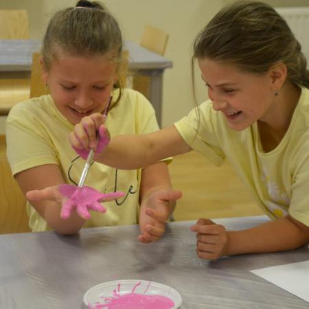 Dziewczynka maluje koleżance dłonie różową farbą