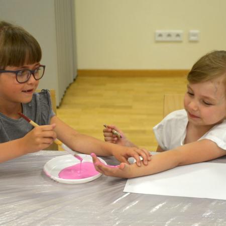 Dziewczynka maluje koleżance dłonie różową farbą