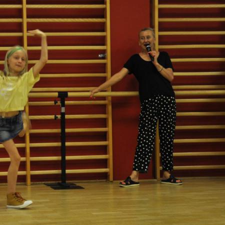 Dziewczynka w akrobatycznej pozie, obok instruktor z mikrofonem