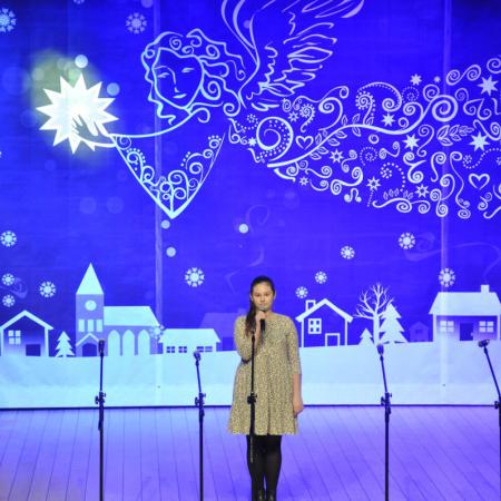 Dziewczynka w jasnej sukience śpiewająca na scenie , w tle Mikołaj