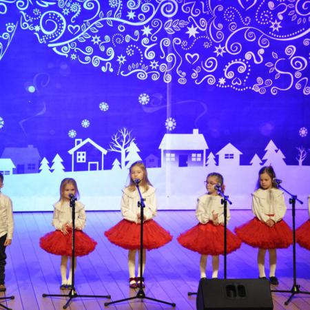 Dziewczynki  w białych koszulkach i czerwonych spódniczkach występują na scenie.
