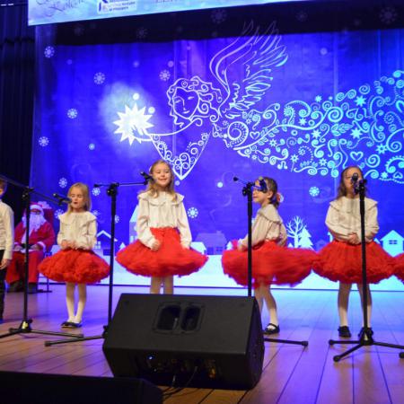 Dziewczynki w białych koszulkach i czerwonych spódniczkach śpiewają na scenie