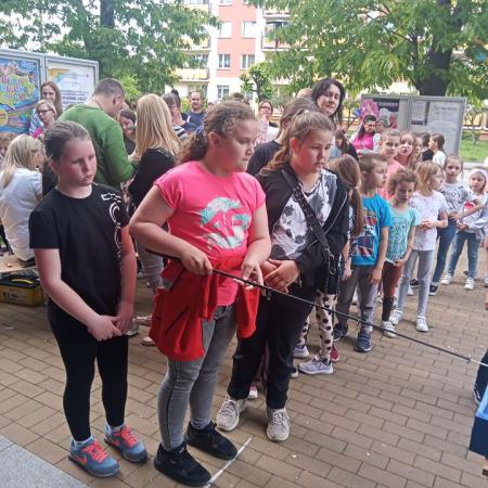 Grupa dzieci stoi w rzędzie do konkursu z wędką.