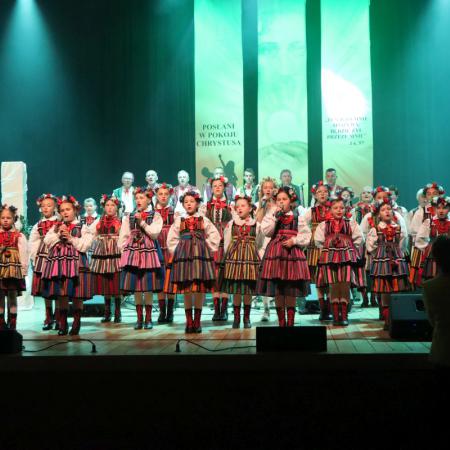 Grupa dzieci w ludowych strojach śpiewa na scenie