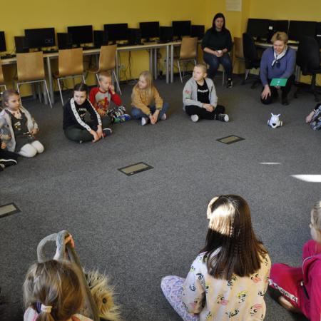 Grupa dzieci wraz z Pania z biblioteki siedzą w kole na dywanie