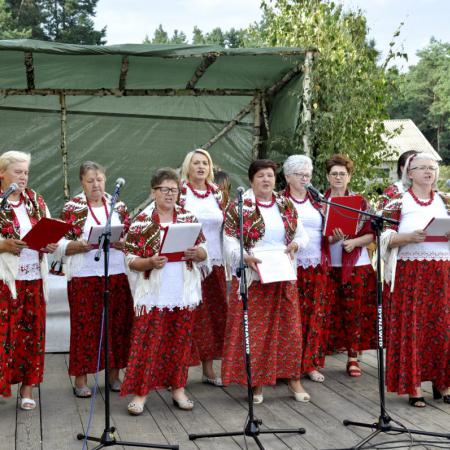 Grupa kobiet w czerwonych sukienkach śpiewają do mikrofonów