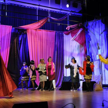 Grupa kobiet w kolorowwych szalach wytśpuje na scenie
