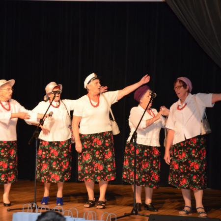 Grupa kobiet w przebraniach tańczą i spiewają na scenie