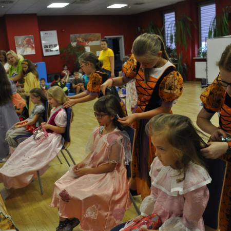Grupa ludzi w kolorowych strojach. Przebrane za czarownice dziewczyny robią fryzury dzieciom.