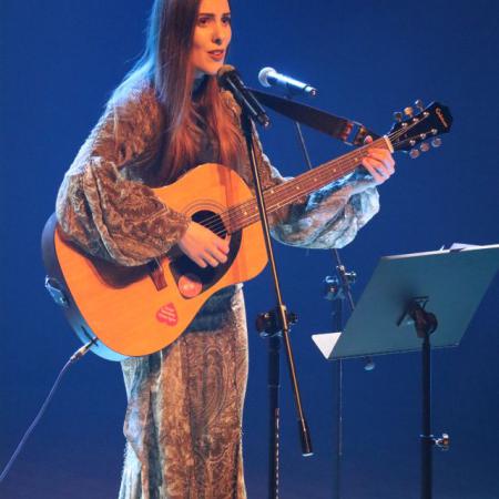 Kobieta gra na gitarze i śpiewa przy mikrofonie podczas koncertu 