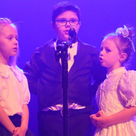 Chłopiec i dwie dziewczynki śpiewają przy mikrofonie na scenie podczas koncertu 