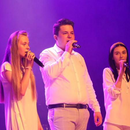 Mężczyzna i dwie kobiety śpiewają przy mikrofonach na scenie